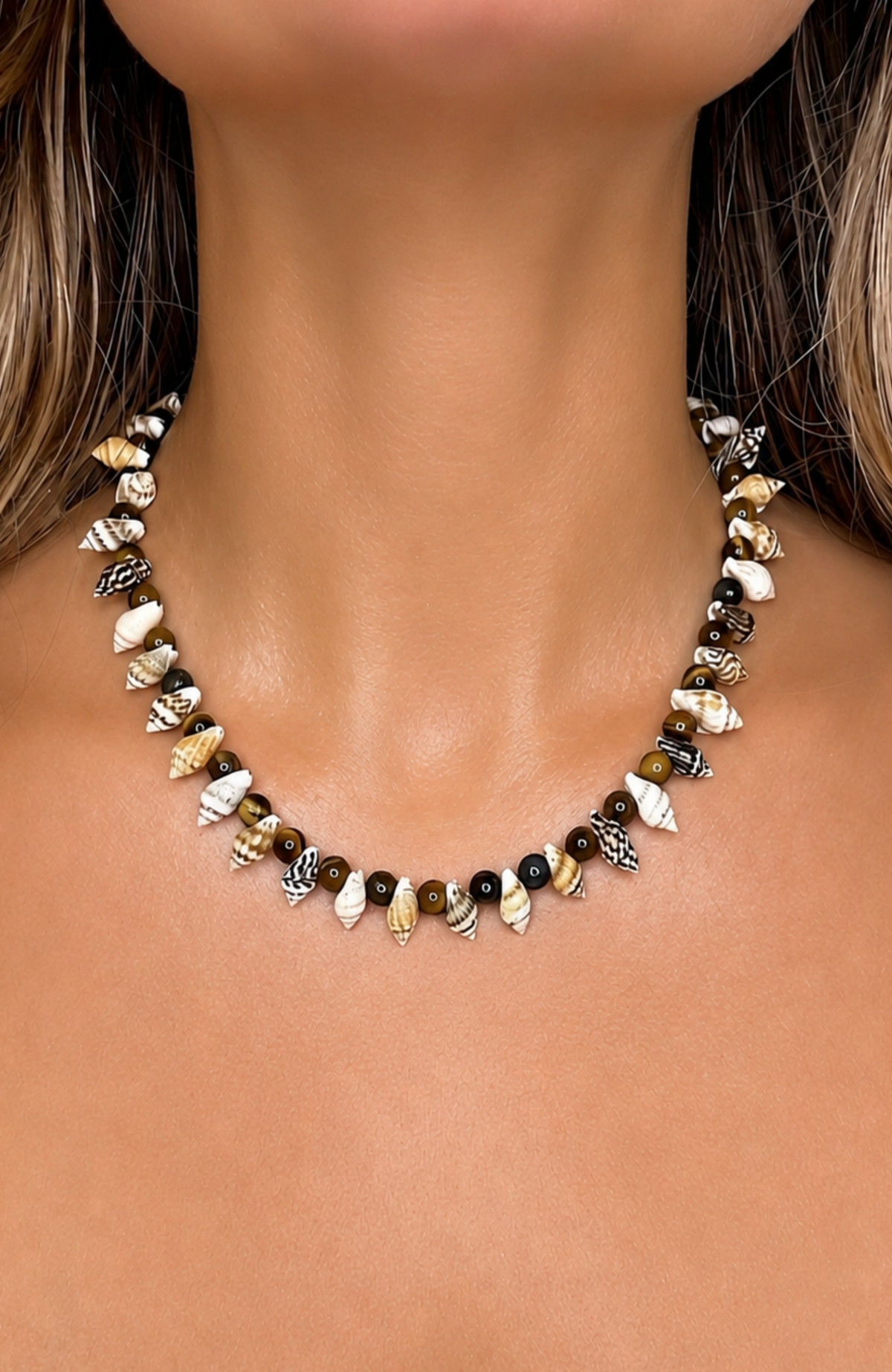 A close-up of a woman's neck and chest wearing a beaded necklace made of small seashells and dark beads.