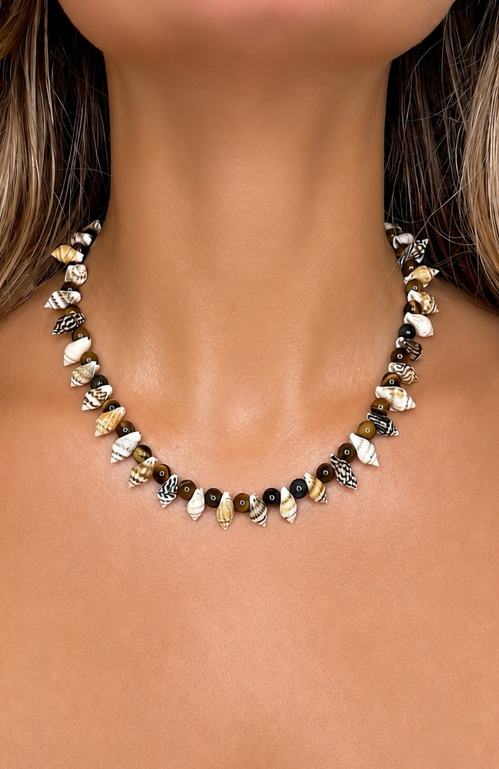 A close-up of a woman's neck and chest wearing a beaded necklace made of small seashells and dark beads.