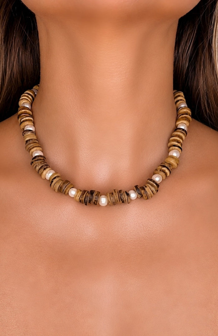 A close-up of a model's neck and upper chest wearing a beaded necklace made of alternating brown coconut beads and pearls.